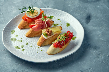 Assorted bruschetta with baked peppers, camembert, prosciutto and lightly salted salmon in a white plate on a gray background