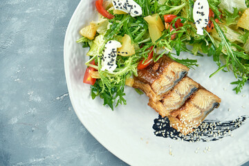 Salad with eel, arugula, leaves and cream cheese in a white plate on a gray concrete background. Seafood salad. Top view