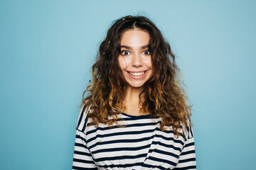 Happy, lovely brunette woman with big brown eyes and beautiful smile looking at camera. Attractive woman wearing white and black striped sweatshort. Isolated over blue background.