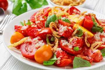 tomato salad with crispy fried onion, quinoa and fresh basil on a white plate on a wooden table, close-up, landscape view from above