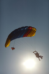 Silhouettes of skydiver tandem instructor and passenger under the parachute canopy against the background of the dazzling sun and blue sky, close-up.