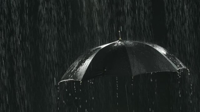 Black umbrella under streams of rain in a dark studio. Close up. Slow motion.