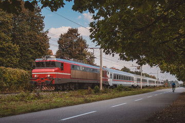 Modern passenger train with red locomotive and white carriages riding on the tracks towards...