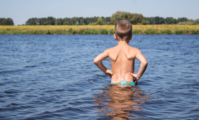 boy stands in the water against the background of a yellow field