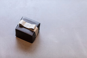 A  gift wrapped in black wrapping paper with a brown bow laying on a grey surface. Minimalistic present for a man during festive season or Christmas