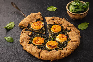 Rustic spinach and goat cheese galette on black background.