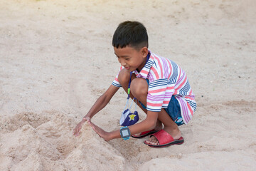 Asian boy playing with sand in a sandcastle shape on the summer beach.