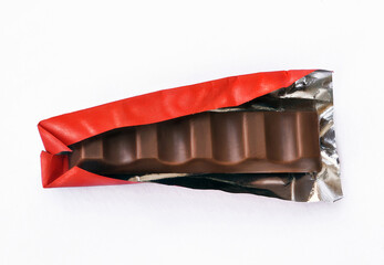 Dark chocolate bar in red opened foil on white background.