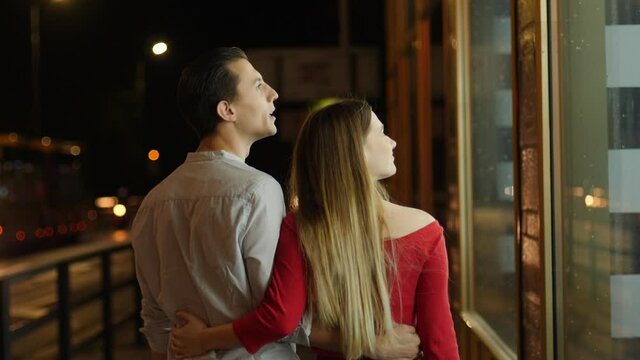 Young happy couple watch store showcase and see expensive thing they wish to buy behing glass frontage during night city walk