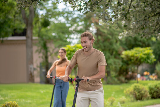 Two Young People Riding Scooters In The Park