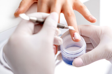 Close up of the process of applying acrylic powder on the nails of a young woman in a beauty salon