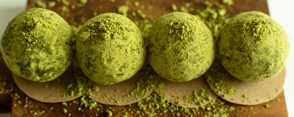 Matcha energy balls dusted with green matcha powder on wooden board. Homemade healthy vegan raw energy truffle balls. 
