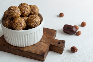 Homemade energy truffle balls in white bowl on wooden board. Raw vegan healthy dessert, date and nuts balls, ingredients.