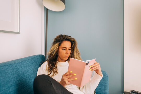 Young woman reading book on sofa
