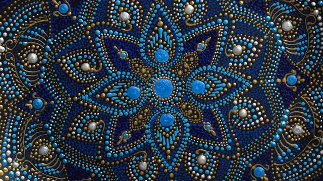Decorative ceramic plate with black, blue and golden colors, painted plate rotating on background, closeup, top view. Decorative porcelain plate painted with acrylic paints, handwork, dot painting