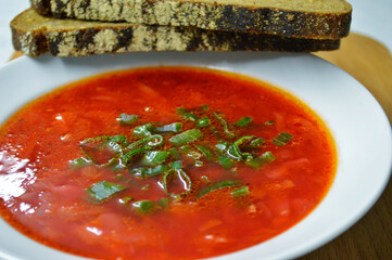 Borscht and two pieces of rye bread on a wooden background.