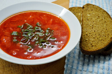 Borscht, two slices of rye bread and a blue napkin in a cage on a wooden background