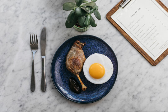 Confit duck leg and fried duck egg on restaurant table
