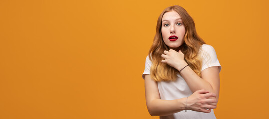 Portrait of the scared girl with wavy redhead, wearing white t-shirt, isolated on yellow background. Copy space