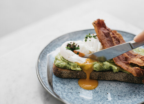 Knife cutting through avocado toast with egg and bacon
