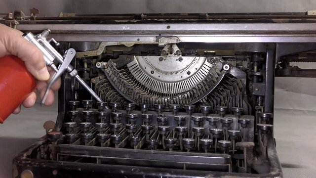 The master greases the old typewriter. A video camera drives by near an old typewriter on a table in a monotone color.
