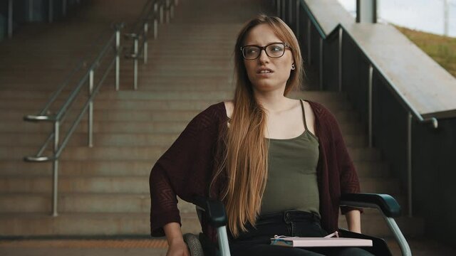 Sad helpless disabled young woman in front of the stairways in the wheelchair. inaccessible area. High quality 4k footage