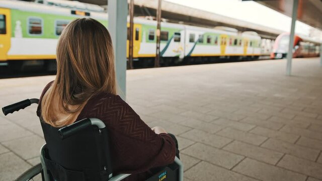 Lonely young caucasian woman in the wheelchair on the train station. High quality 4k footage