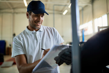 Happy car mechanic taking notes while examining stock of tires in auto repair shop.