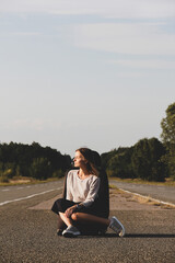 A beautiful girl sits on the background of the road and sky. Girl and nature