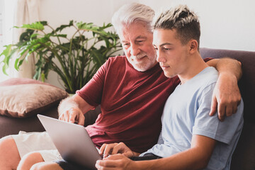 A white haired grandfather and teenage grandson are looking at the same laptop computer sharing the same passion or interest - friendship and family love concept