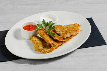 Potatoes pancakes with adjika, sour cream are on a plate on a light wooden background.  Restaurant menu.  National Ukrainian cuisine.