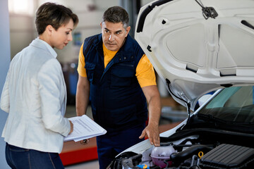Auto repairman explaining car engine malfunction to a businesswoman in a workshop.