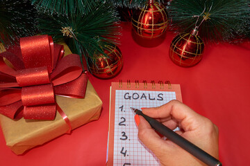 A young woman writes a list of goals for the current year with a pen in a notebook, next to a New...