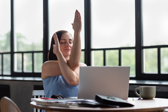 Caucasian woman at room with her crossed arms doing yoga exercise resting during working day. Garudasana, Eagle pose.