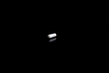 One white tablet capsule on black background, search for medicines, fight against diseases and for...