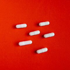 White tablets capsules on a red background, search for medicines, fight against diseases and for health, search for a remedy for coronovirus