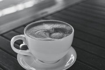 Cup with coffee on the table. Sugar in the foam of the drink. Black white shot