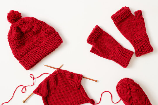 Knitting Project In Progress. Winter Hat And Mittens Knitted With Red Yarn On White Background.