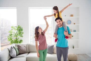 Photo of positive cheerful three people mom dad play weekend game carry shoulders small kid girl hold hand in house indoors