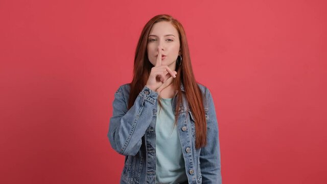 Girl showing to be quiet with finger, isolated on red background.