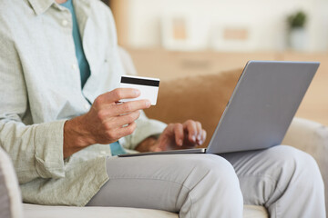 Close-up of man sitting on sofa with laptop on his knees he shopping online with credit card