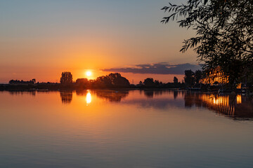 The light of the rising sun above lake Noordhovense plas is beautifully reflected in both the water and the windows of the adjacent houses