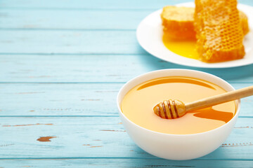 Bowl of honey with honeycomb on blue wooden table