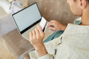 Close-up of young man holding credit card and paying online for purchases using laptop computer