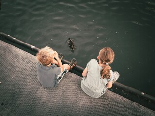 Zwei Kinder sitzen am Hafenbecken und beobachten eine schwimmende Ente