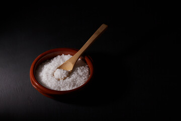 Coarse, white salt in a red bowl and a wooden spoon. All on a black background