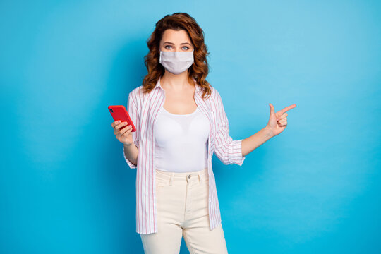 Portrait of her she nice attractive lovely wavy-haired girl using gadget app 5g showing copy space advert point covid news wear medical mask isolated on blue color background