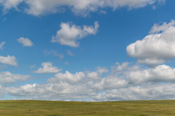 bright white fluffy clouds in blue sky with green field, open space