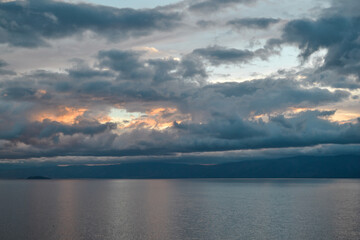 evening bright orange pink sunset with silvery gray blue clouds on lake baikal with a mountains ridge on the horizon