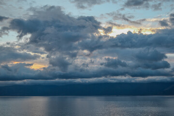 evening bright sunset with silvery gray blue clouds on lake baikal with a mountains ridge on the horizon